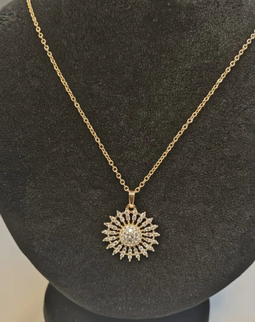 Gold necklace with a sunflower-shaped pendant on a black stand.